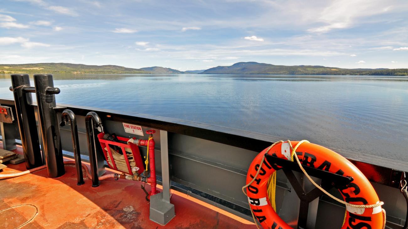 View from onboard a ferry with lifebuoy, overlooking a calm lake and distant hills.