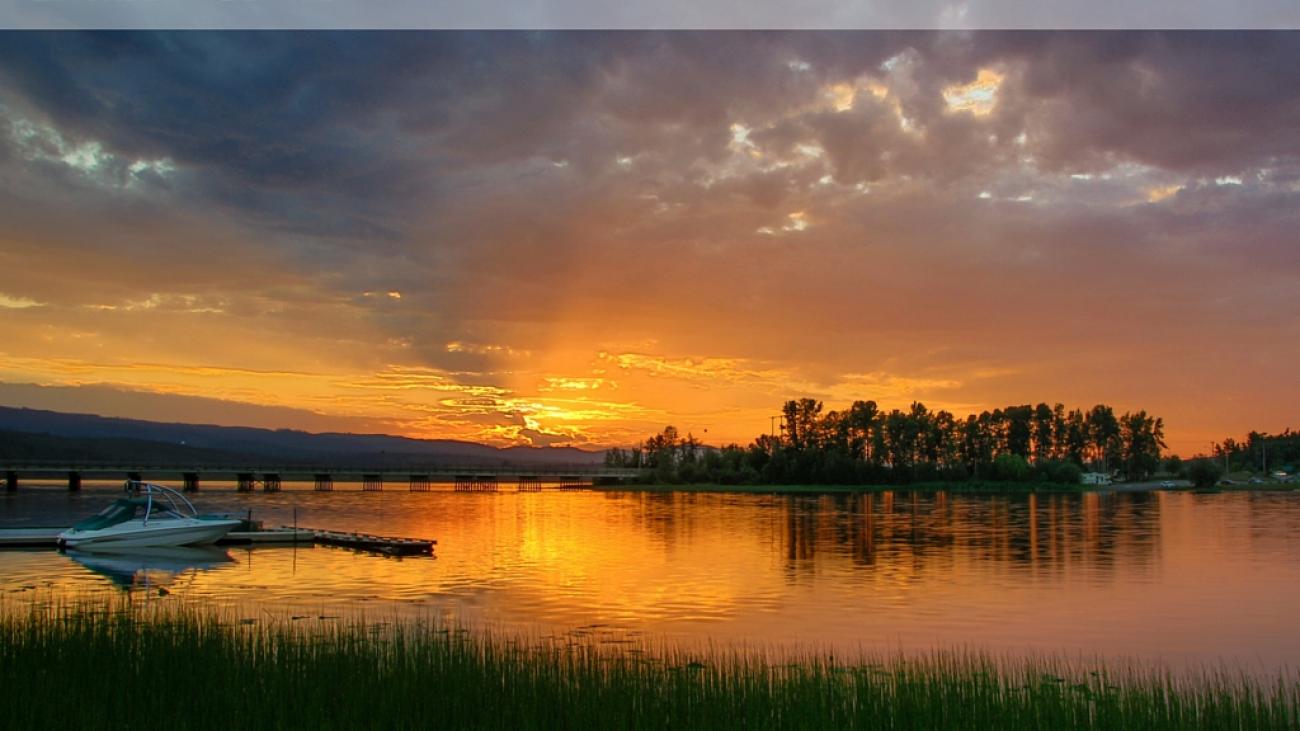 Dramatic orange sunset over Burns Lake with a boat dock and forested shoreline.