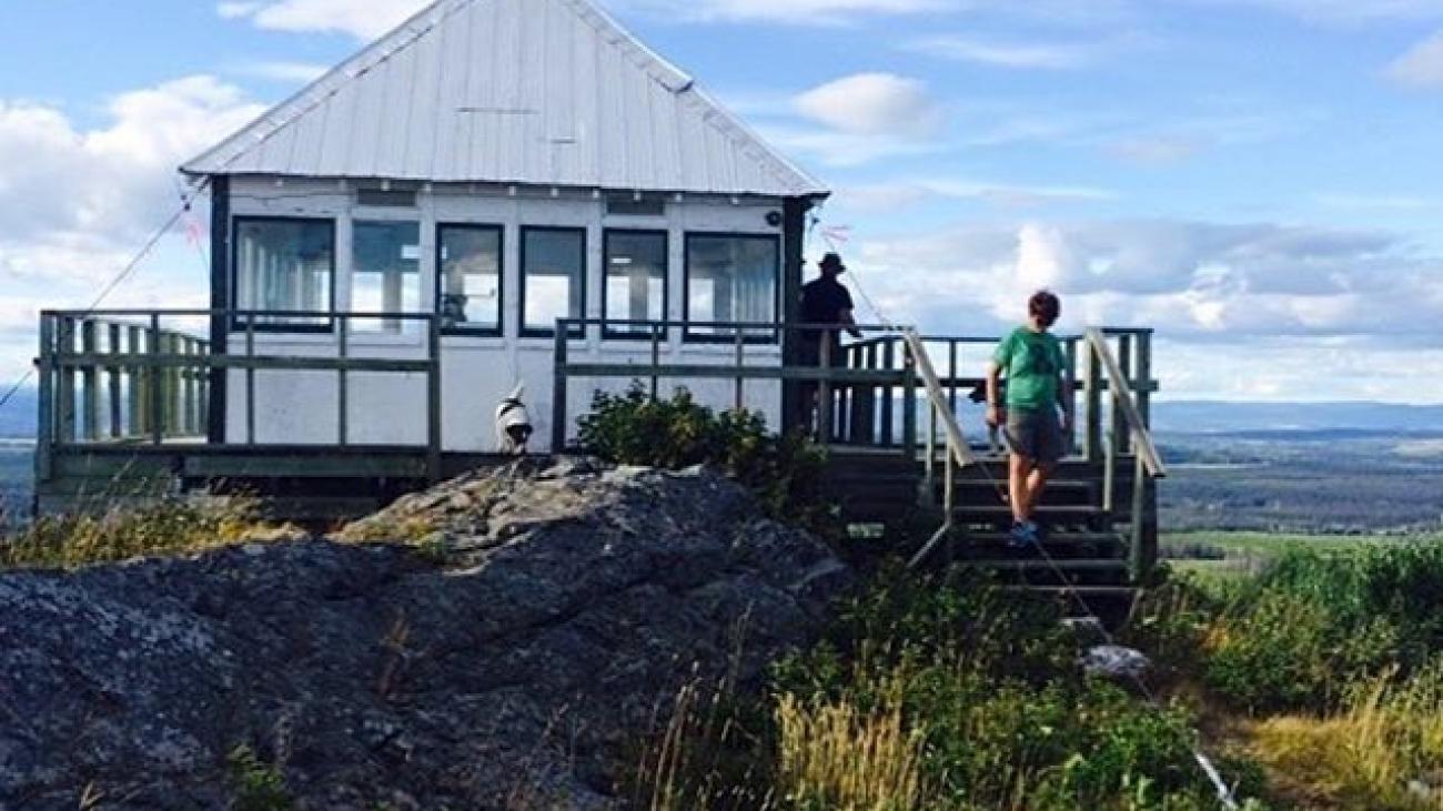 Fire lookout tower on a rocky hill. Two people are at the lookout tower.