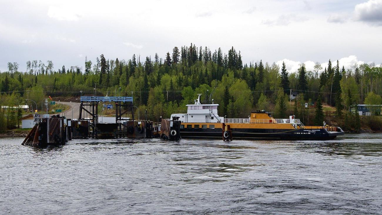 Cable ferry docked at landing near forested shoreline and rural road access.