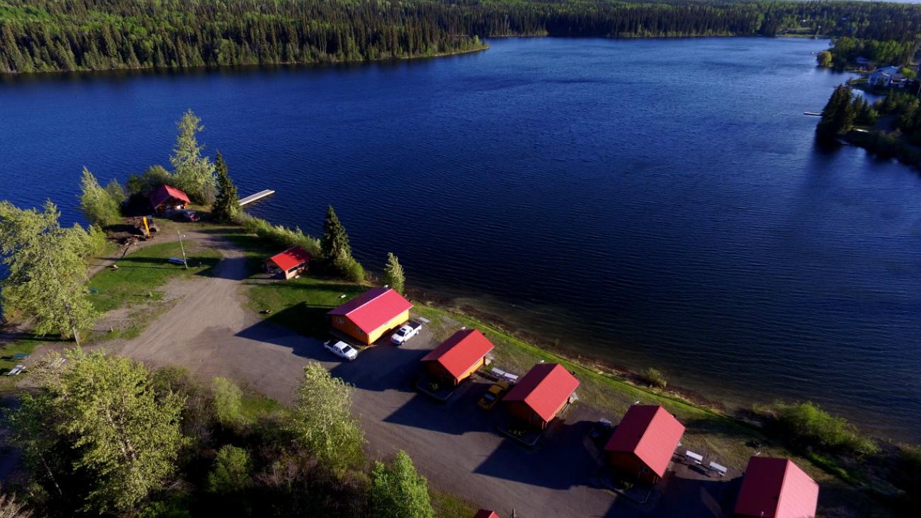 Aerial view of lakeside cabins with red roofs surrounded by trees.