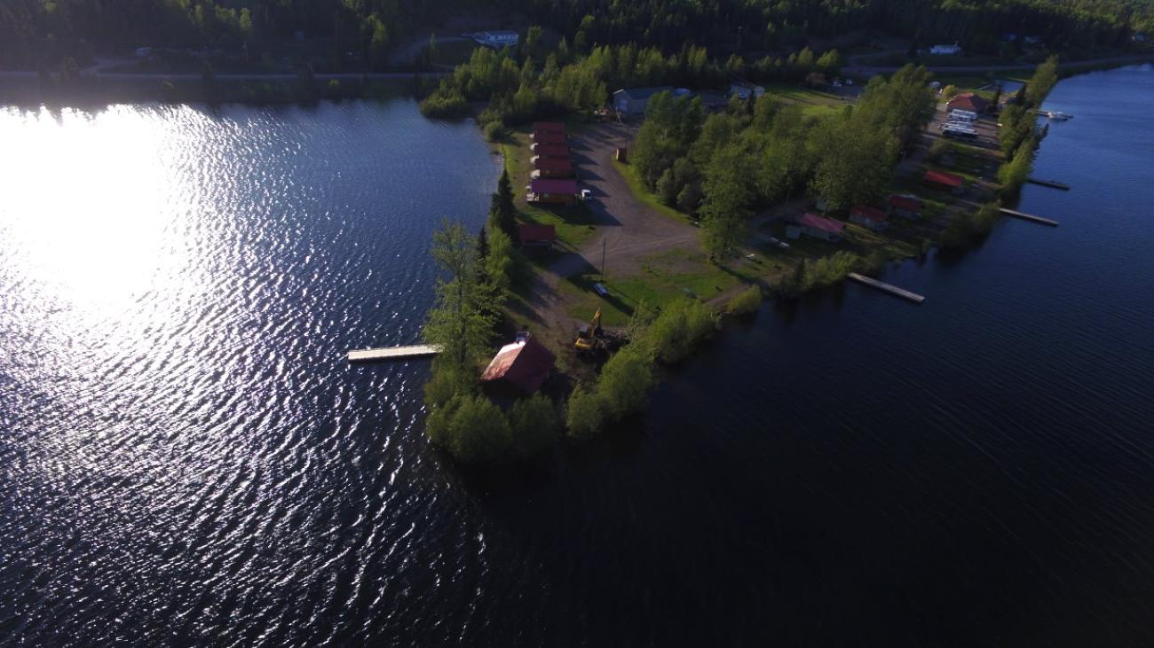 Aerial view of a small peninsula with trees and cabins by a calm lake.