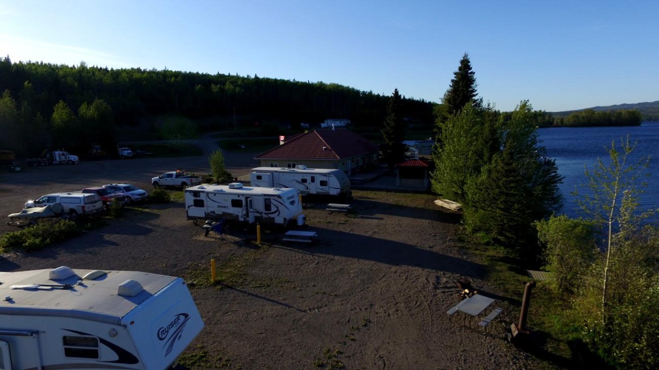 Campsite with RVs by a lake at sunset, surrounded by trees.
