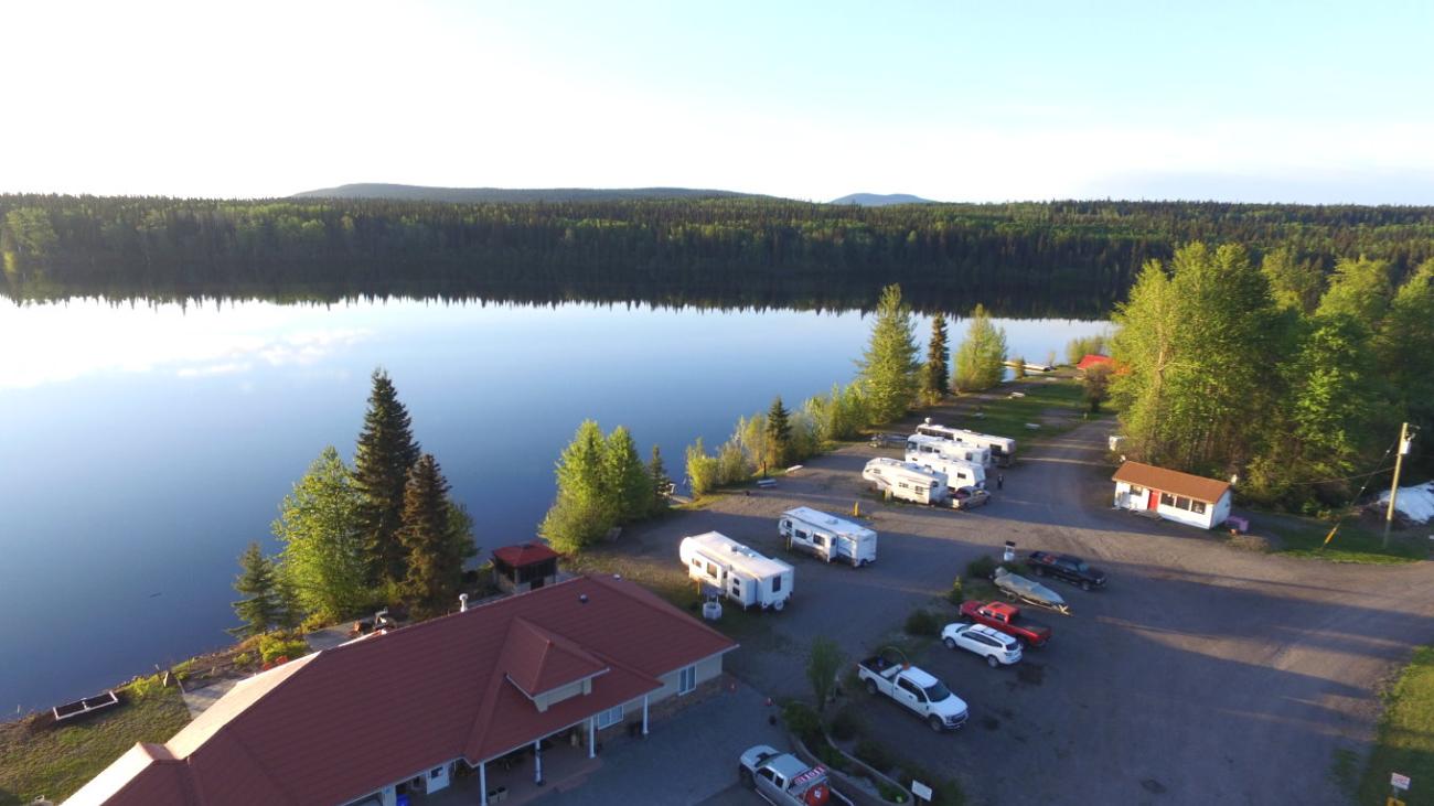 Lakeside lodge with parked cars and RVs in a forested area.