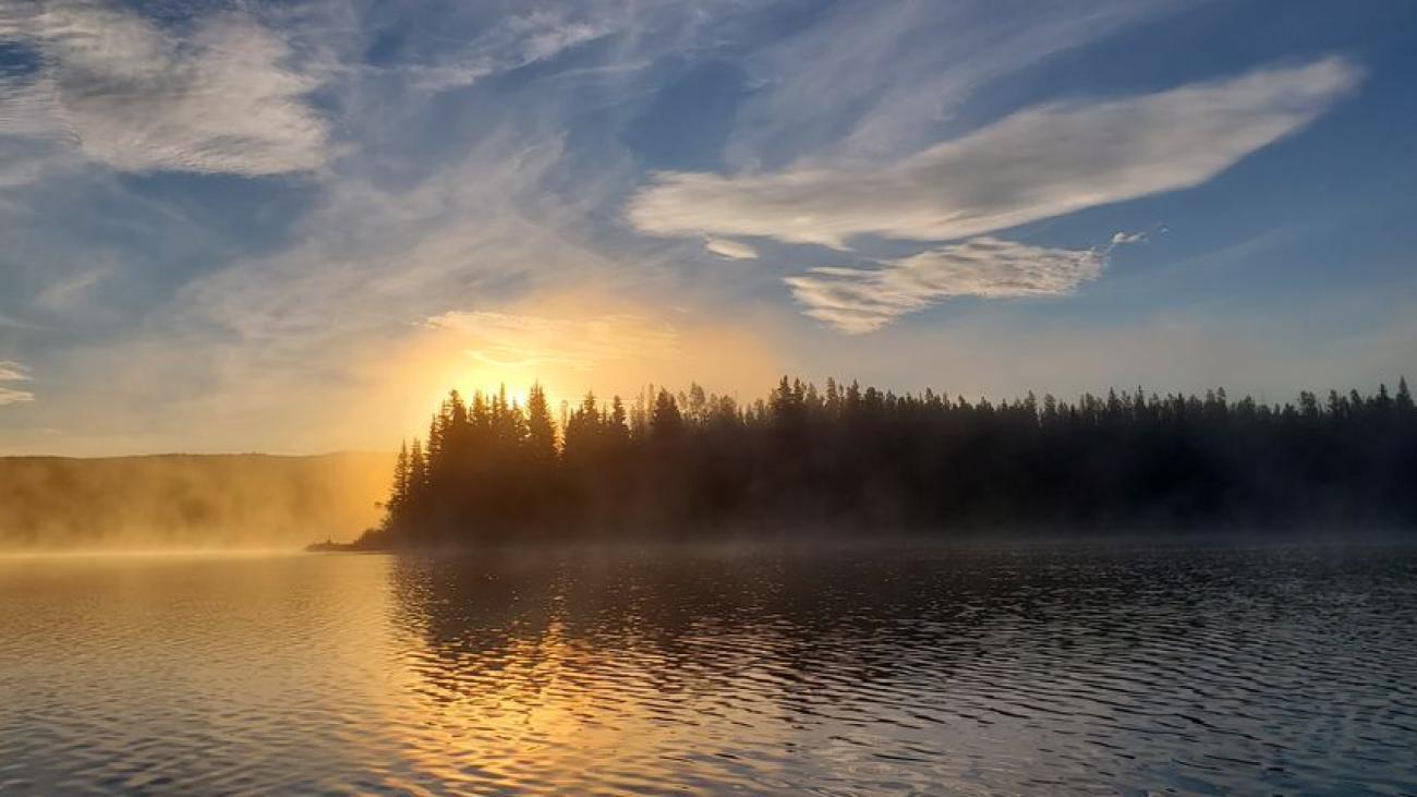 Full moon reflecting on a tranquil lake under a night sky with clouds and stars.