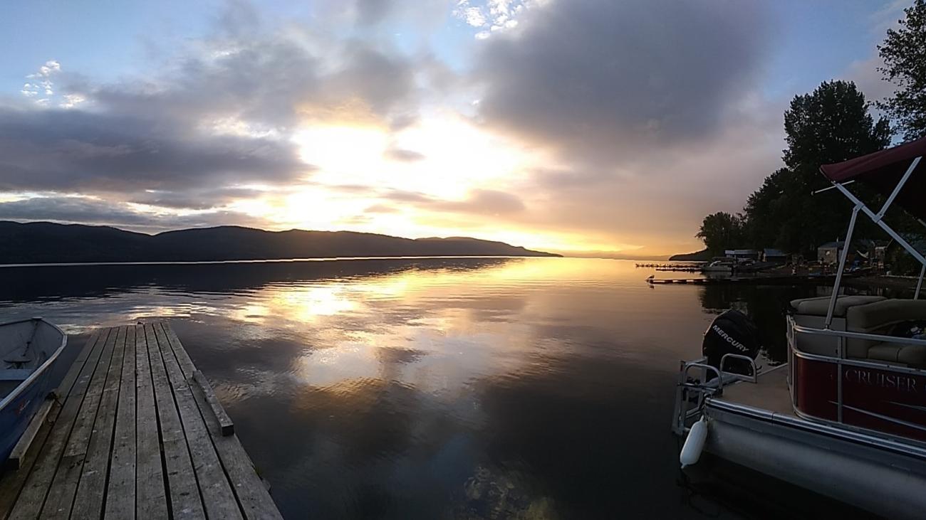 Colorful sunset sky over a still lake with dark hills and soft clouds.