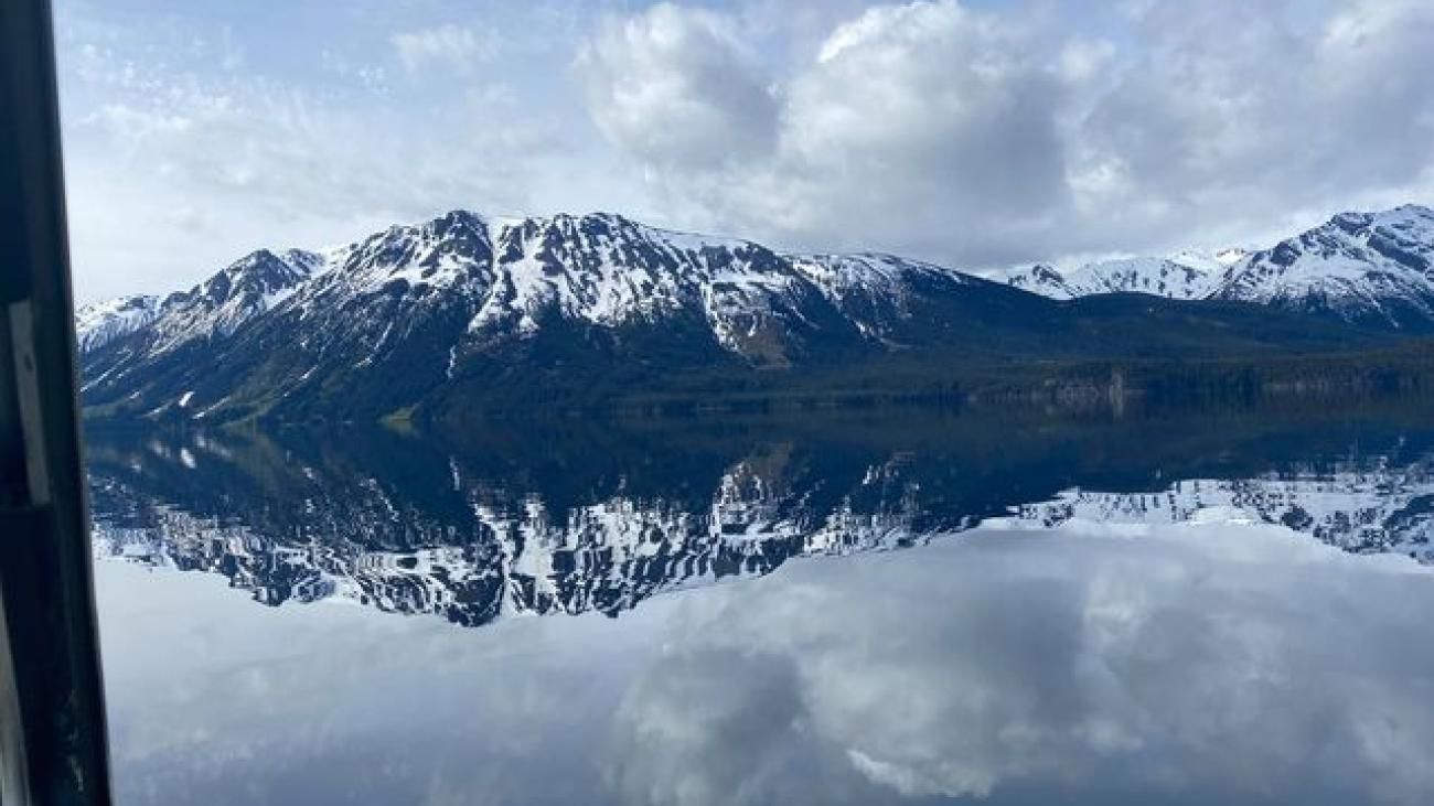 Fishing rod bent over calm mountain lake with distant snow-capped peaks.