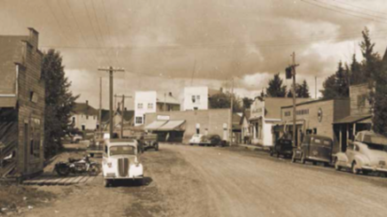 Sepia-toned photo of vintage downtown street lined with classic cars and wooden storefronts.