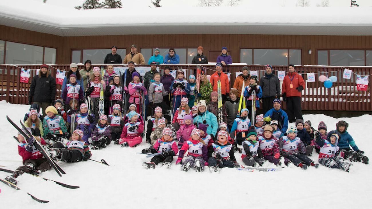 Large group of kids and adults posing after a snowy ski event.