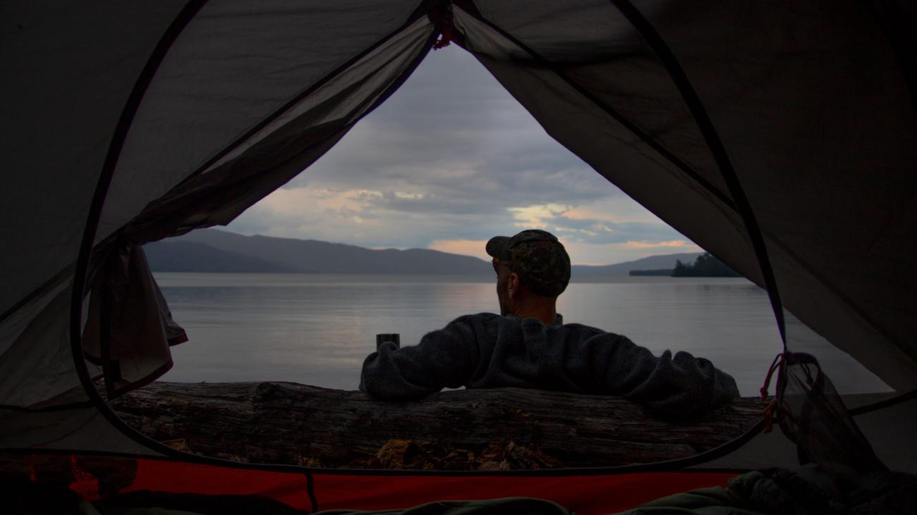 Camper’s view from inside a tent looking out at a calm lake and cloudy sky.