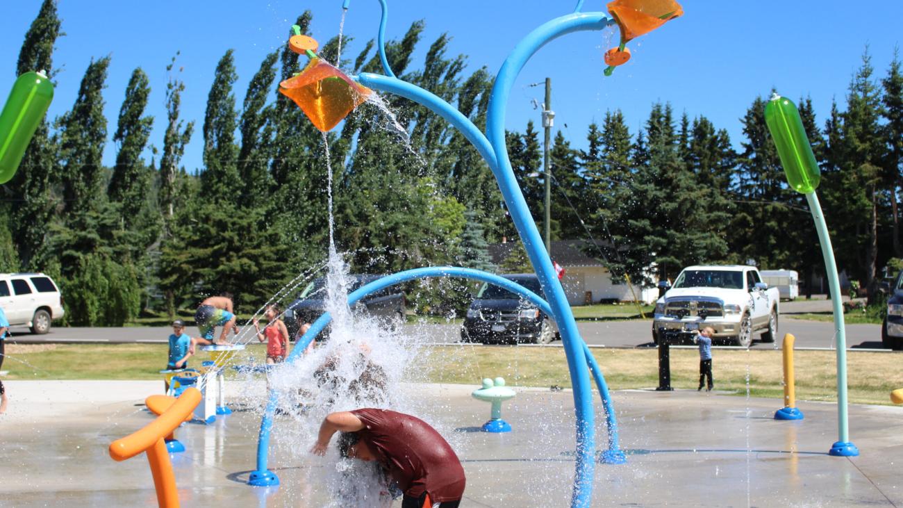 Kids playing under water features at a colorful splash park on a sunny day. Image