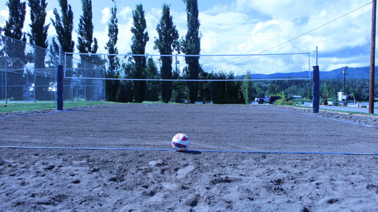 Sand volleyball court with net and a volleyball placed at the center.