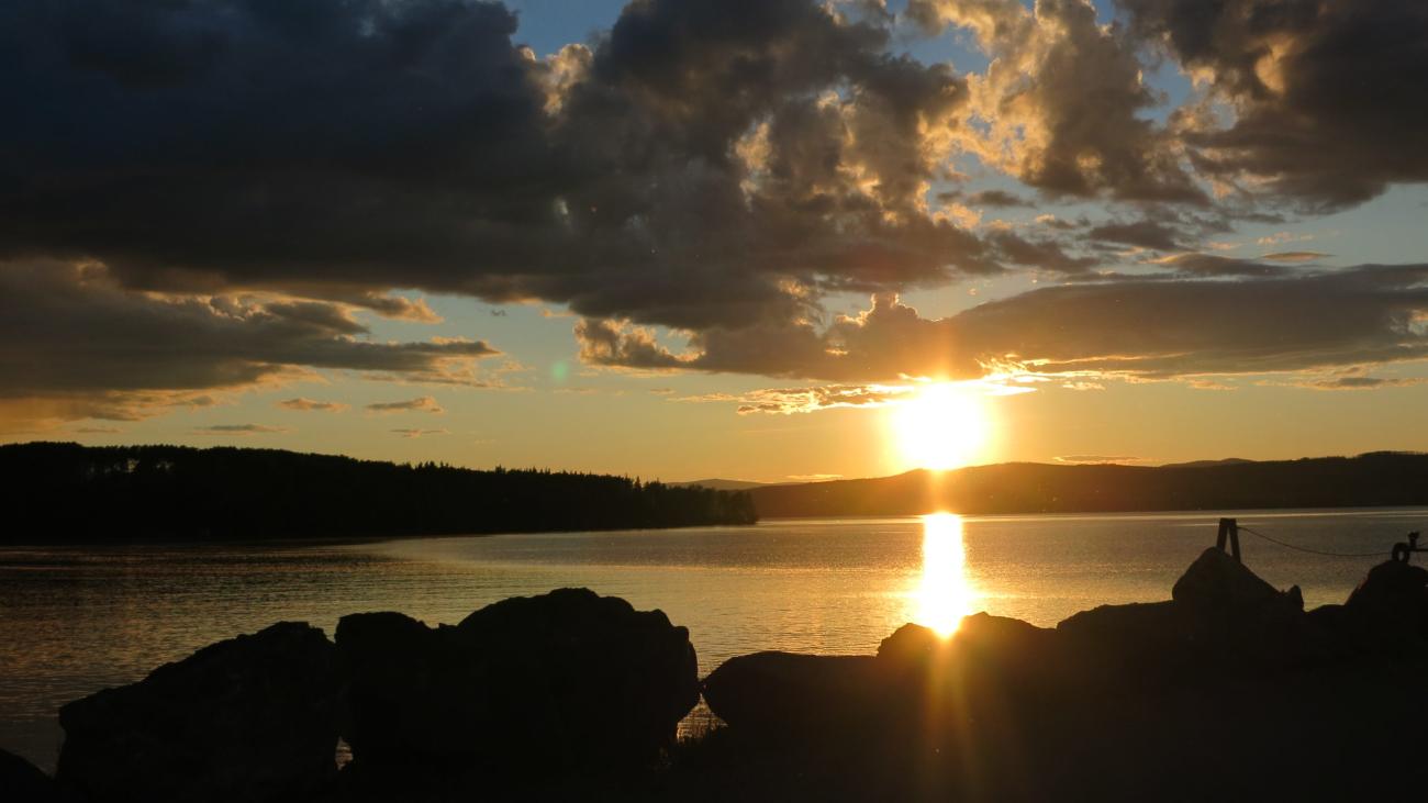 Glowing sunset over lake with dramatic clouds and silhouetted rocks in foreground.