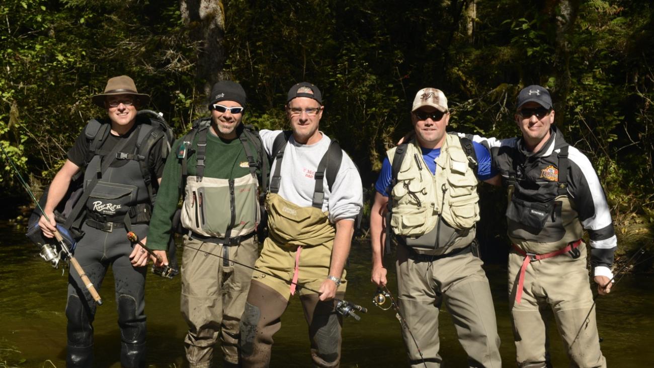 Five men in fishing gear standing by a forest stream.