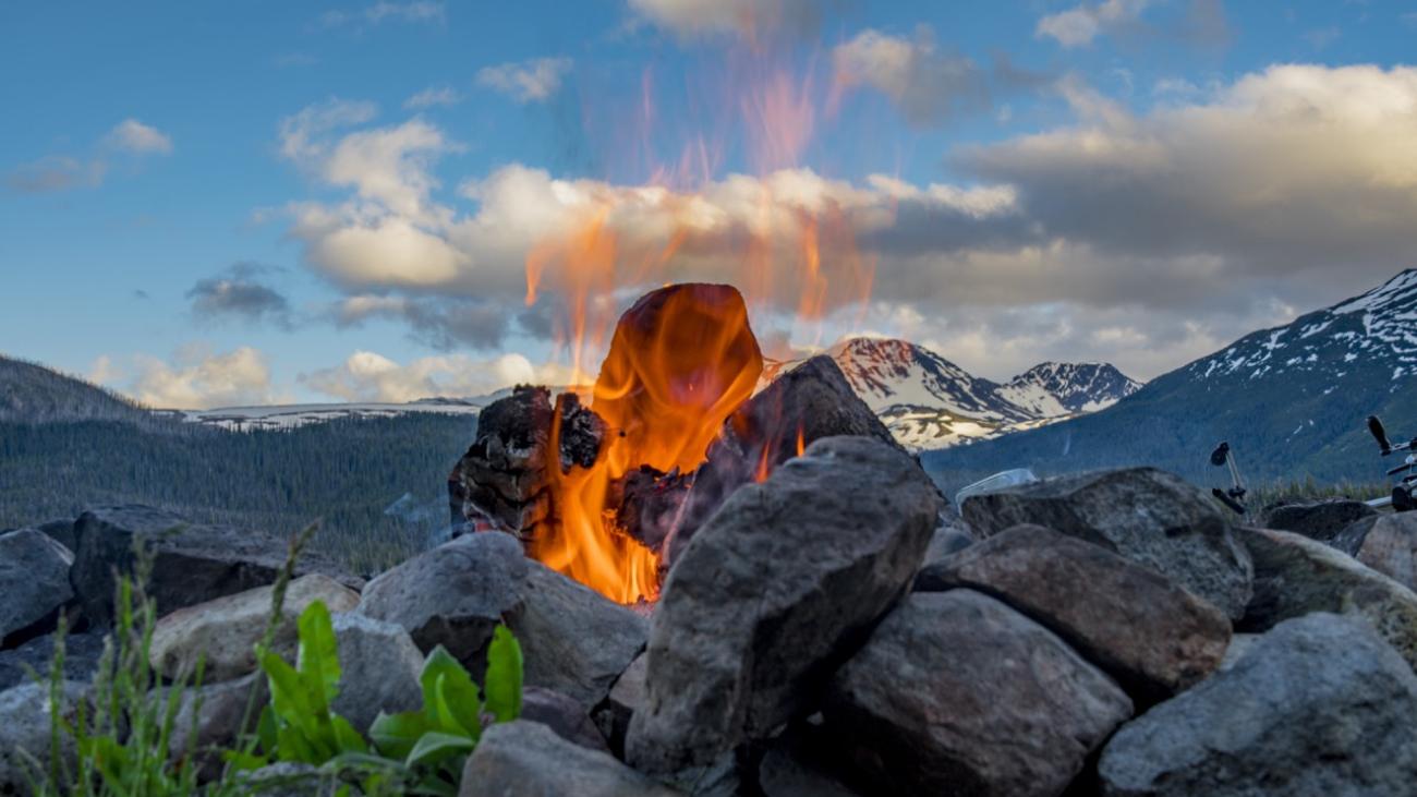 Rock ring with fire against a mountain backdrop under a blue, cloudy sky.