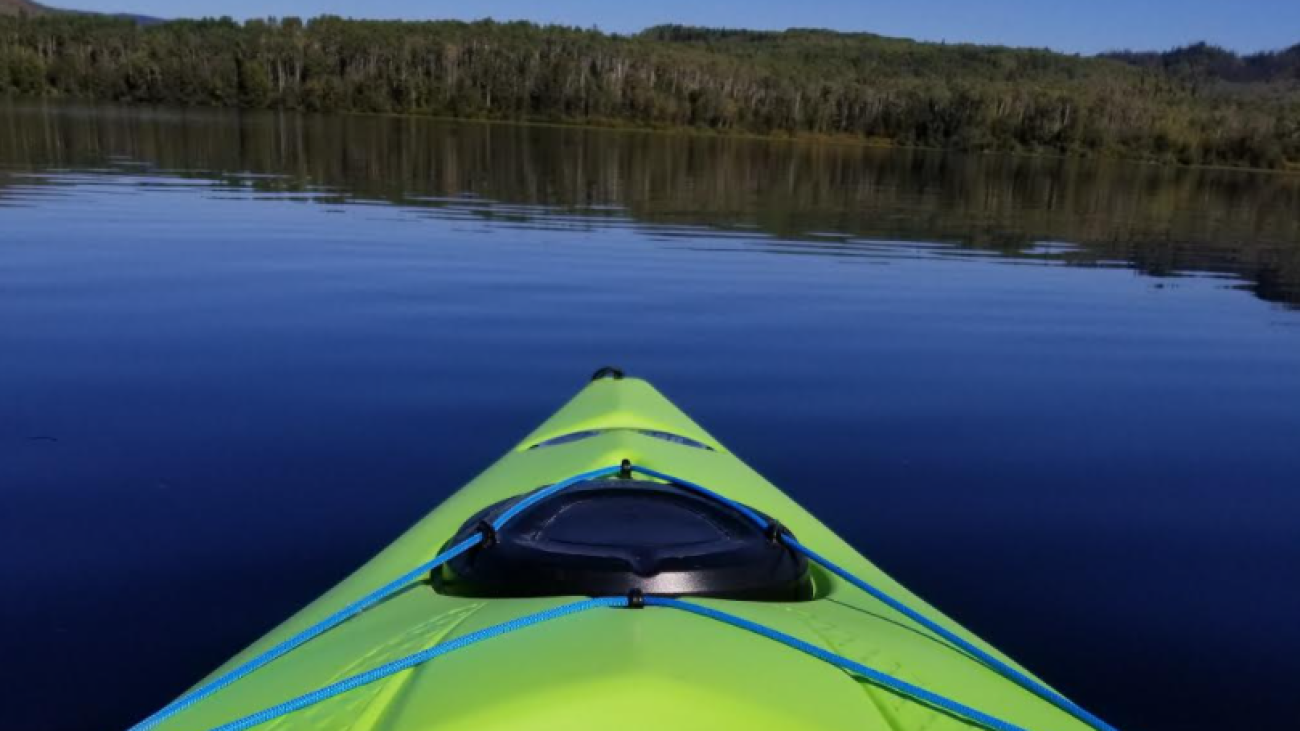 Bright green kayak floating on a perfectly still lake with forest in the distance.