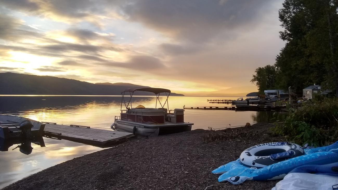 Lakeside dock with pontoon boats and inflatable floaties at sunset.
