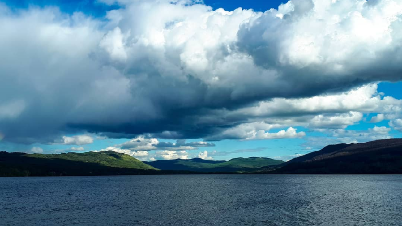 Deep blue lake under dramatic cumulus clouds rolling over green hills.