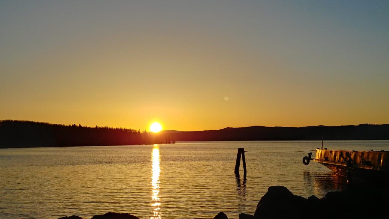 Tranquil golden sunset casting reflection on lake near wooden dock.