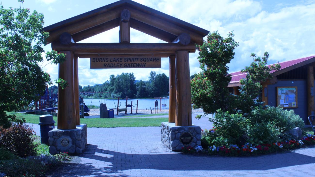 Wooden entrance archway at Burns Lake Spirit Square with a view of the lake beyond.
