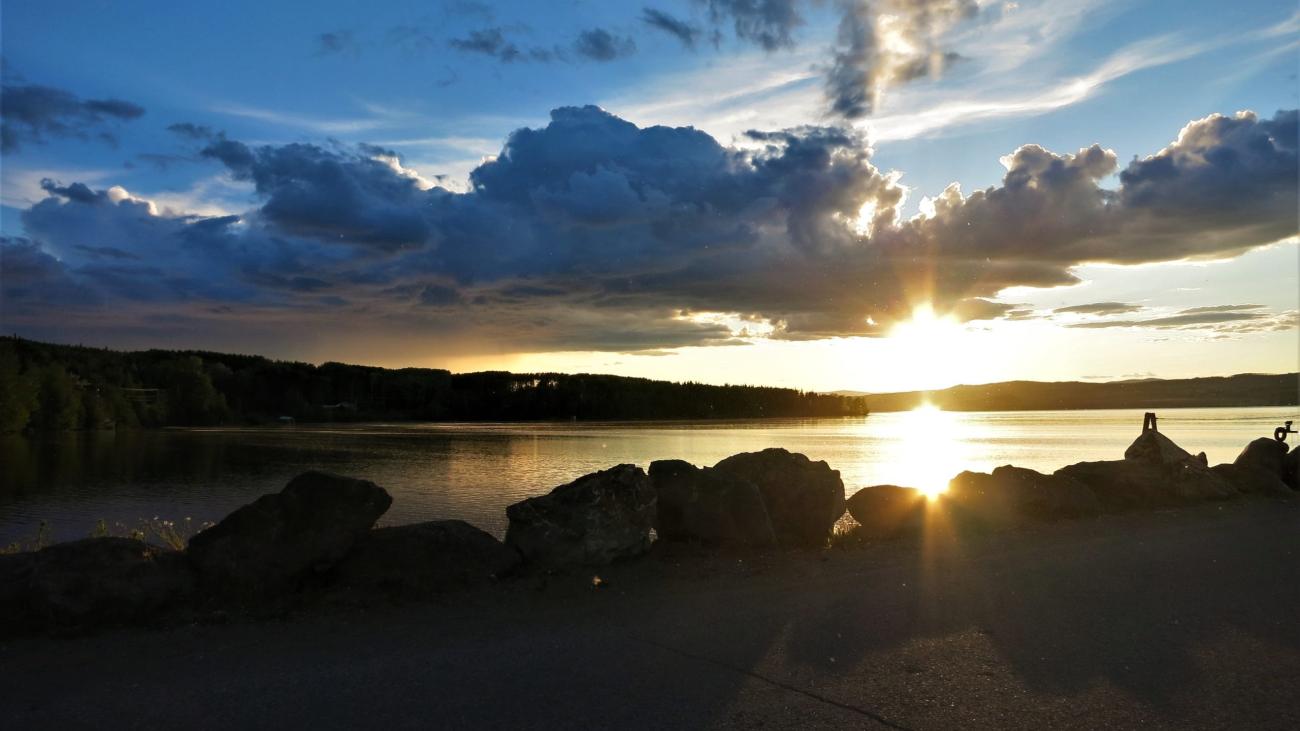 Early snowfall lining a lakeside road with autumn foliage and cloudy skies.