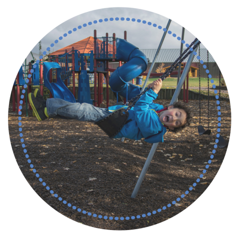 Child swinging joyfully at a playground with colourful equipment.